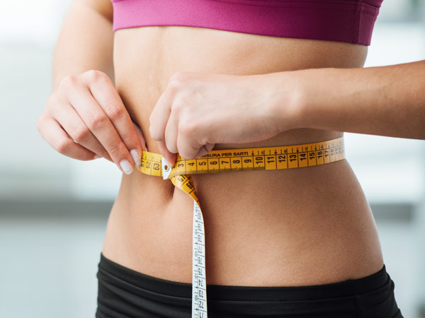 A person measuring their waist with a tape measure, symbolizing progress in weight loss and fitness goals.